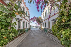 A narrow street flanked by buildings with large windows and green shutters, leading to a white building with a visible entrance. - Vacation Studio 'Vv Faro' with Mountain View, Wi-Fi and Air Conditioning (Puerto de Mogán)