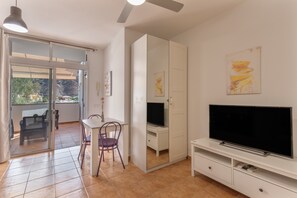 Ein Zimmer mit einer Schiebetür, die auf einen Balkon führt, einem Fernsehgerät auf einem weißen Schrank und einem Gemälde an der Wand.