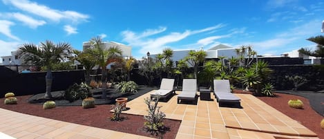 A patio with lounge chairs, a tiled floor, and various plants.
