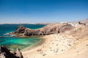 A coastal beach with rocky cliffs, clear turquoise waters, and a sandy shore populated with people. - Vacation Villa 'Adais' with Private Pool, Wi-Fi and Air Conditioning (Playa Blanca)