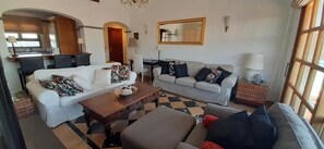 A living room with two sofas, a coffee table, a chandelier, a dining area with chairs, and a kitchen visible through an archway. - Vacation Villa 'Adais' with Private Pool, Wi-Fi and Air Conditioning (Playa Blanca)