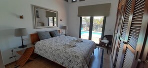 Ein Schlafzimmer mit Bett, Nachttischen, einem Spiegel und Blick auf einen Pool.