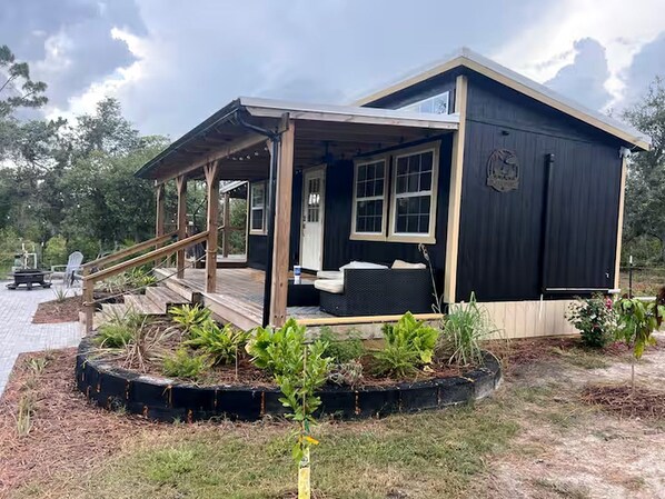 A wooden cabin with a porch, a small deck, and a garden area with plants.