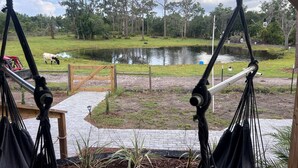 A hammock chair in a covered area with a view of a pond and a grassy field. - Off-Grid, Lakeside Tiny Home in Punta Gorda, Florida, Perfect for a Weekend Getaway (Punta Gorda)