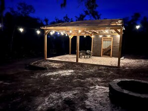 A covered outdoor seating area with a wooden structure, a fire pit, and string lights. - Off-Grid, Lakeside Tiny Home in Punta Gorda, Florida, Perfect for a Weekend Getaway (Punta Gorda)