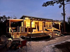 A wooden cabin with a porch, a fire pit, and a chair.