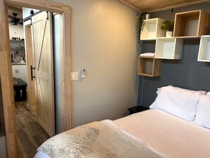 A bedroom with a bed, a wooden door, and a wall-mounted shelf with a plant.