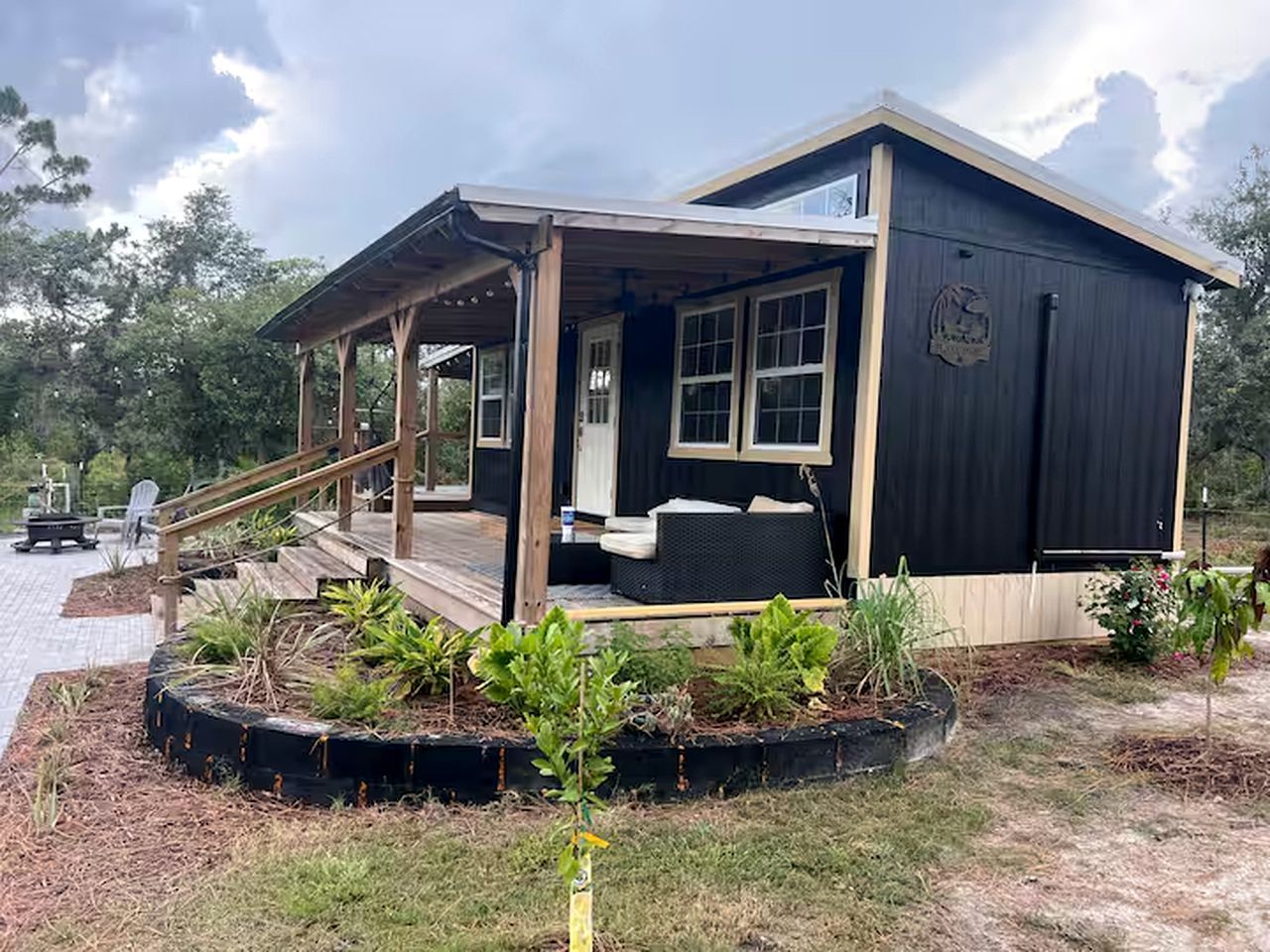 Une cabane en bois dotée d’un porche, d’une petite terrasse et d’un jardin avec des plantes.