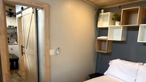 A bedroom with a bed, a wooden door, and a wall-mounted shelf with a plant. - Off-Grid, Lakeside Tiny Home in Punta Gorda, Florida, Perfect for a Weekend Getaway (Punta Gorda)