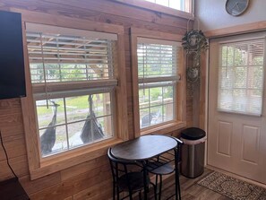 A room with wooden walls, a table with two chairs, a trash can, and a door with a window.