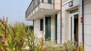Un bâtiment doté d’un balcon, d’une porte avec une enseigne et d’un jardinier avec des plantes.
