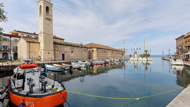 Un port de plaisance avec des bateaux amarrés, une tour imposante et des bâtiments historiques le long de la promenade.