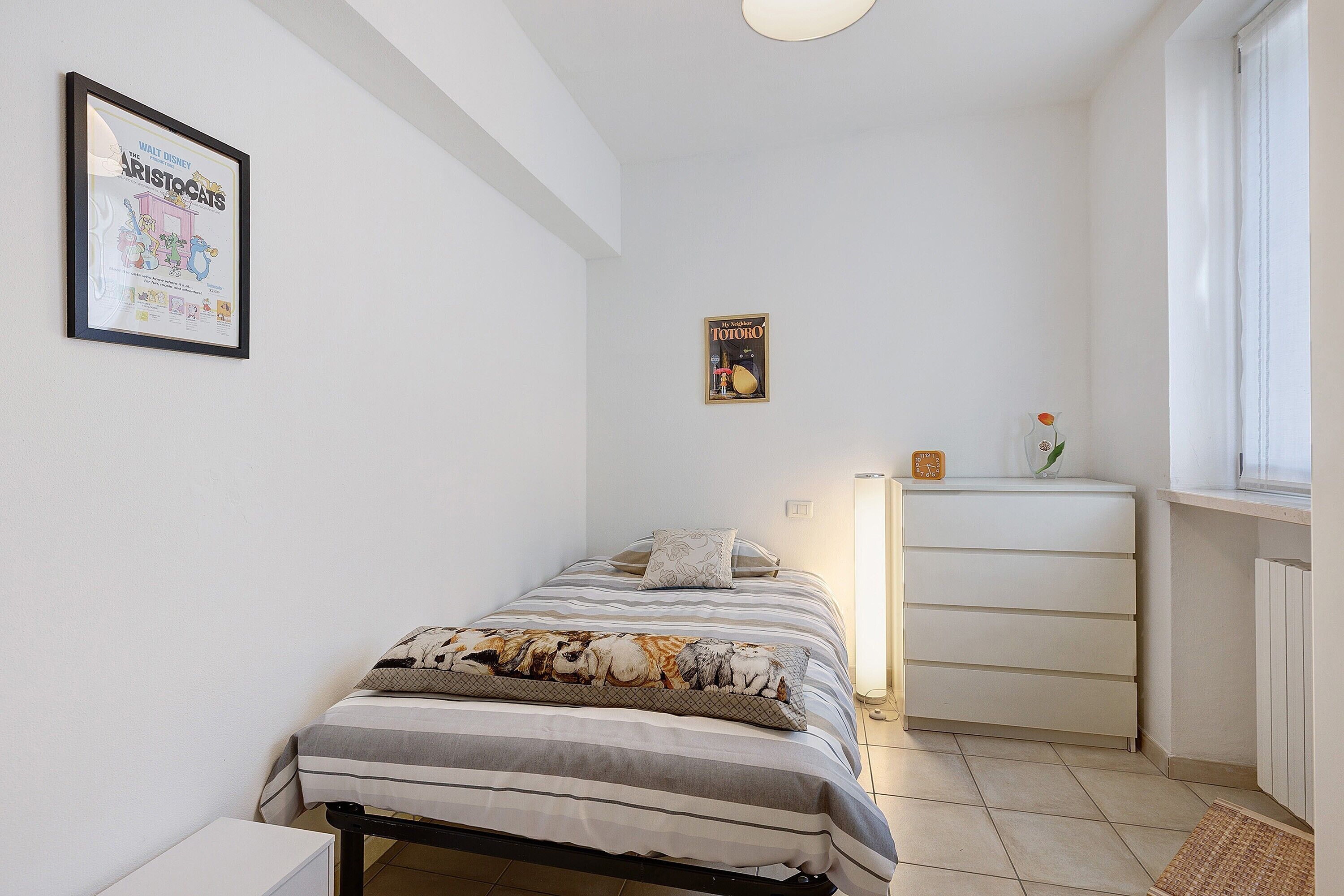 Ein Schlafzimmer mit Bett, Kommode, einem Poster an der Wand und einem Fenster.