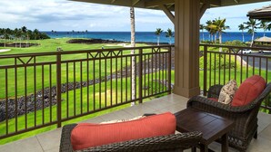 Un balcón con mobiliario de mimbre, vistas a un campo de golf y a la playa.