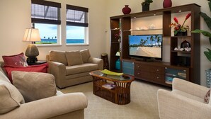 Una sala de estar con sofá, sillones, una mesa de centro, televisor y una estantería con adornos.