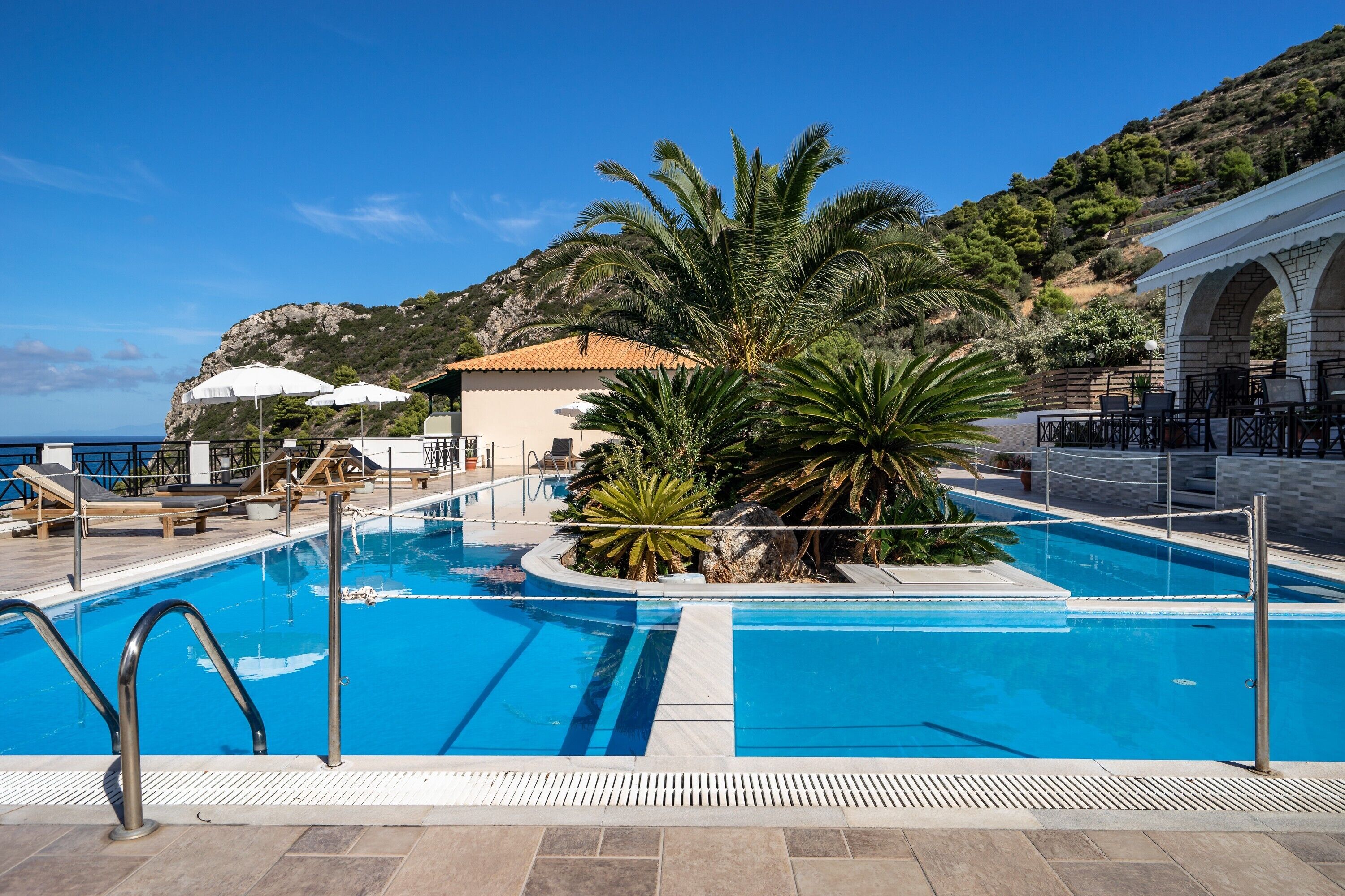 Une piscine avec des chaises longues, un palmier et un bâtiment doté d’un toit en tuiles.