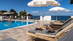 Zona de piscina con sillones reclinables, sombrillas y vista despejada al mar.
