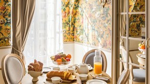 A dining area with a round table set for breakfast, featuring croissants, fruit, and orange juice. - Merveil Signature Suite - Alfred (Paris)