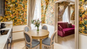 A dining area with a round table and chairs, a vase with flowers, and a red sofa in the background. - Merveil Signature Suite - Alfred (Paris)