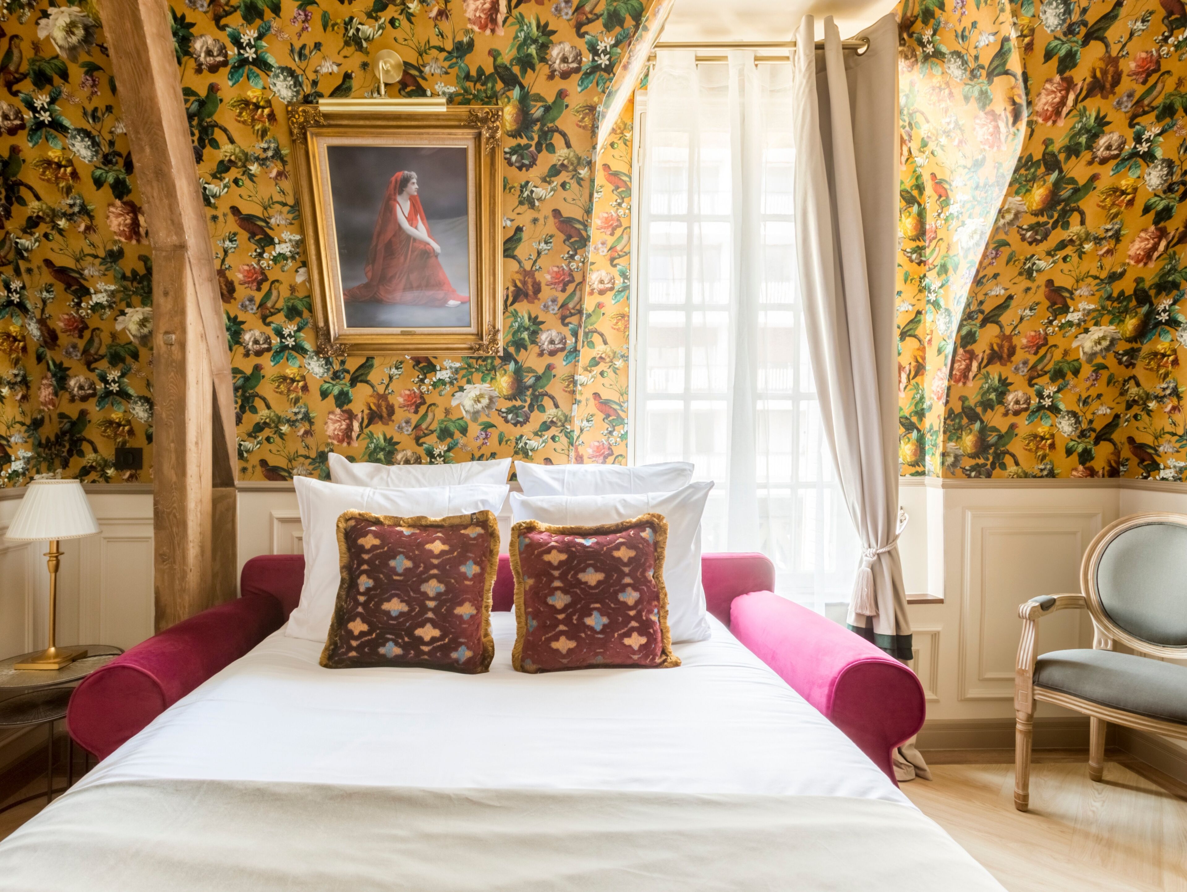 A room with a bed, floral wallpaper, a framed picture, and a chair.