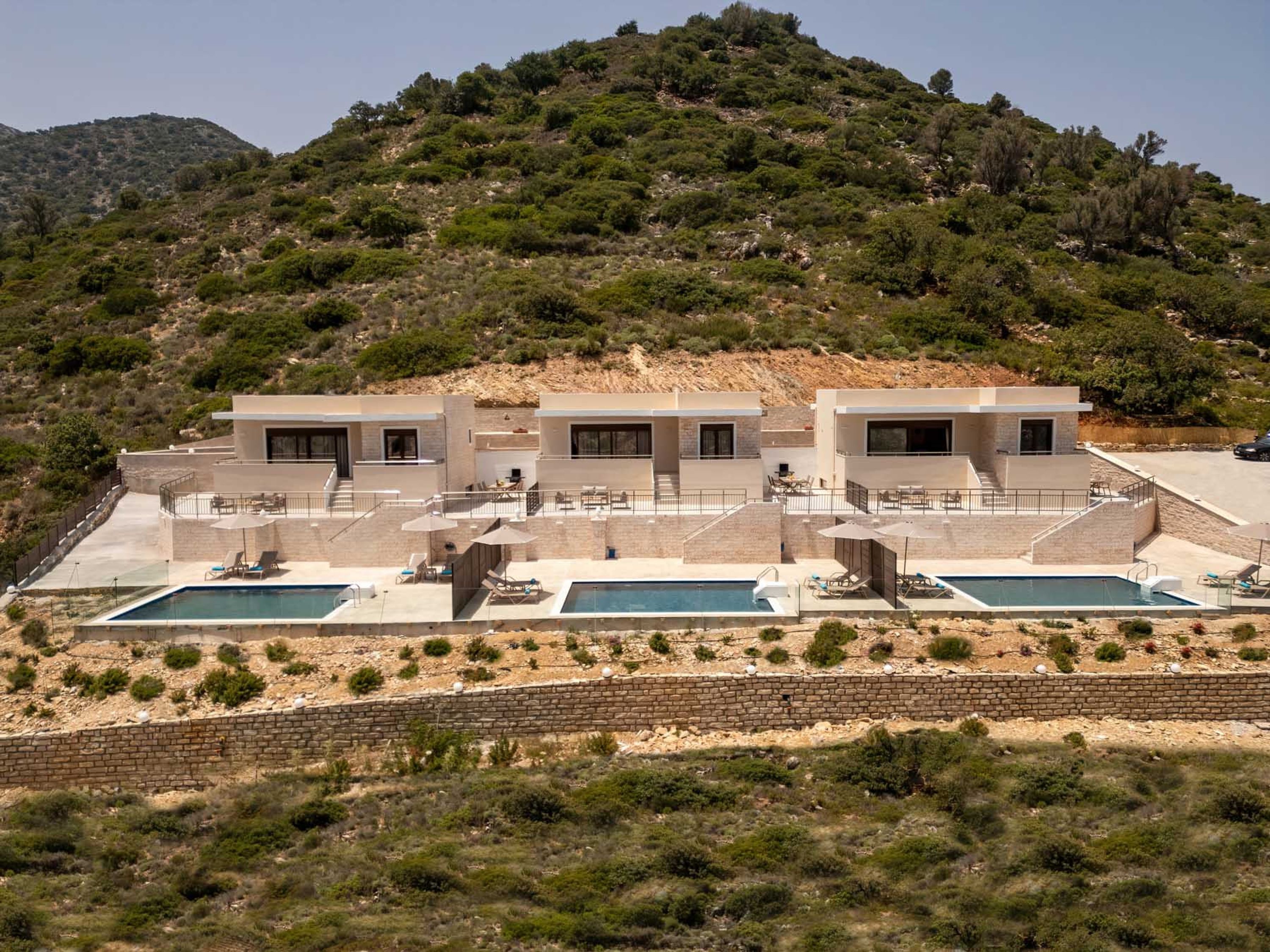 Eine moderne Villa mit Poolbereich, Sitzgelegenheiten im Freien und Blick auf eine hügelige Landschaft.