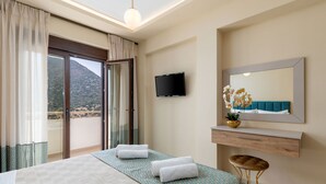 Ein Hotelzimmer mit Bett, Fernseher, Spiegel im Badezimmer, einem Fenster mit Vorhängen und Blick auf eine Berglandschaft.
