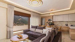 Ein modernes Wohnzimmer mit einer Couch, einem kleinen runden Tisch und Blick auf eine Berglandschaft durch große Fenster.