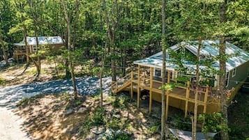 A cabin with a deck and a covered porch, surrounded by trees.