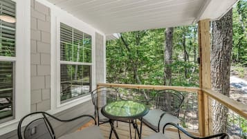 A covered outdoor seating area with a table and chairs, surrounded by wooden railings and large windows.