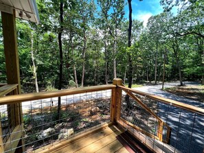 A wooden deck with a metal railing overlooking a forested area.