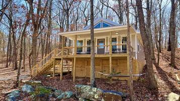 Une cabane dotée d’une terrasse en bois, d’un escalier et d’une grande fenêtre.