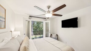 Un dormitorio con dos camas, un ventilador de techo, una televisión y un balcón con vistas a árboles.