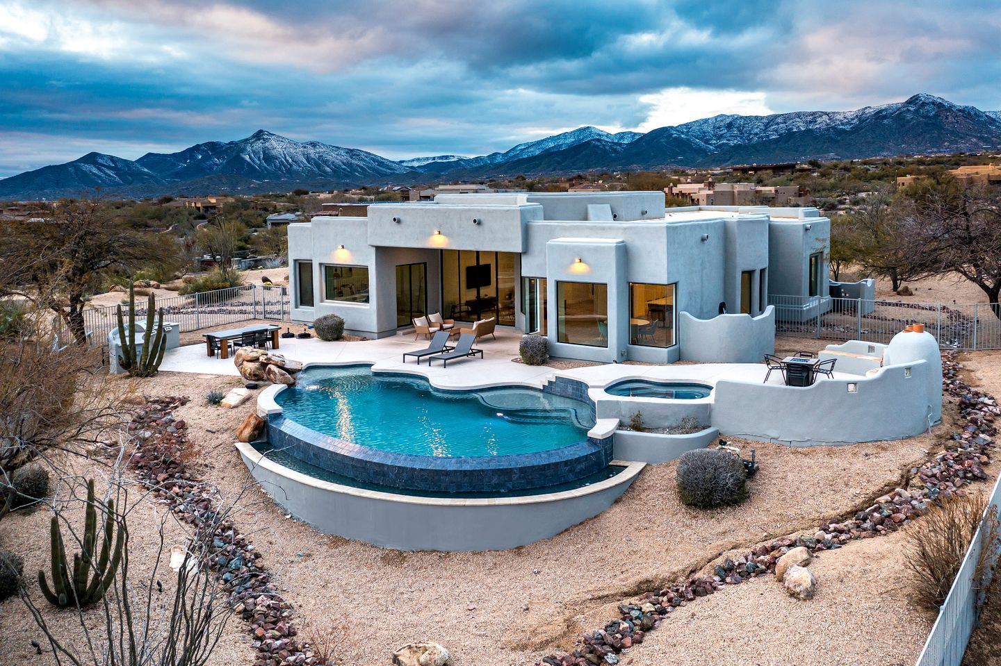 A modern house with a pool, surrounded by mountains and desert landscape.