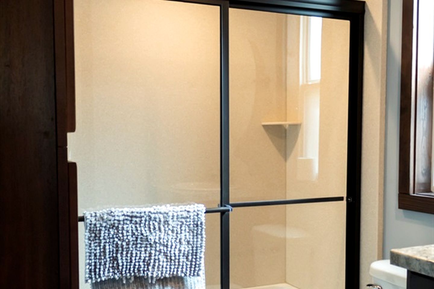 A bathroom with a glass shower enclosure, a towel hanging on a rack, and a marble countertop.
