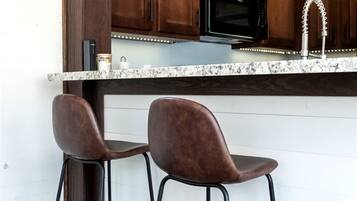 A kitchen with wooden cabinets, a black microwave, a stainless steel faucet, and two bar stools.