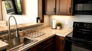 A kitchen with granite countertops, a stainless steel sink, a black stove, wooden cabinets, and a flat-screen TV mounted above the counter.