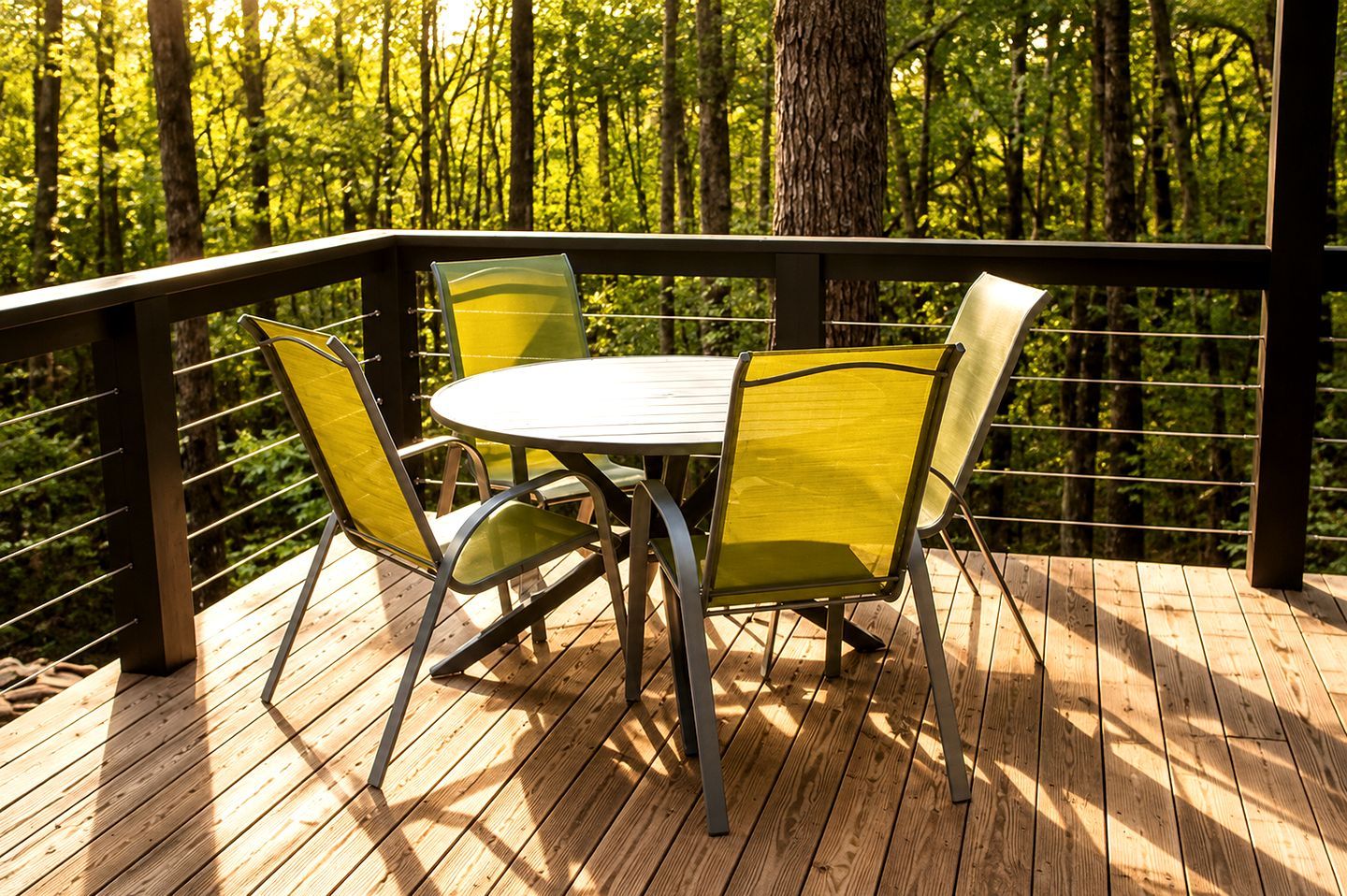 A wooden deck with a table and chairs, surrounded by a metal railing, overlooking a forest.