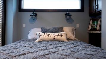 A bed with a quilted cover and a pillow with the text 'Be Our Guest.'