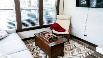 A room with a white sofa, a wooden coffee table with a tray of items, a chair with a red throw, and a patterned rug.