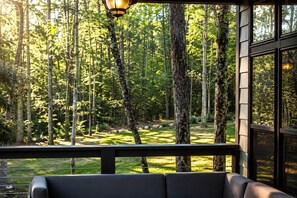 A porch with a view of a forest, a bench, and a hanging light fixture.