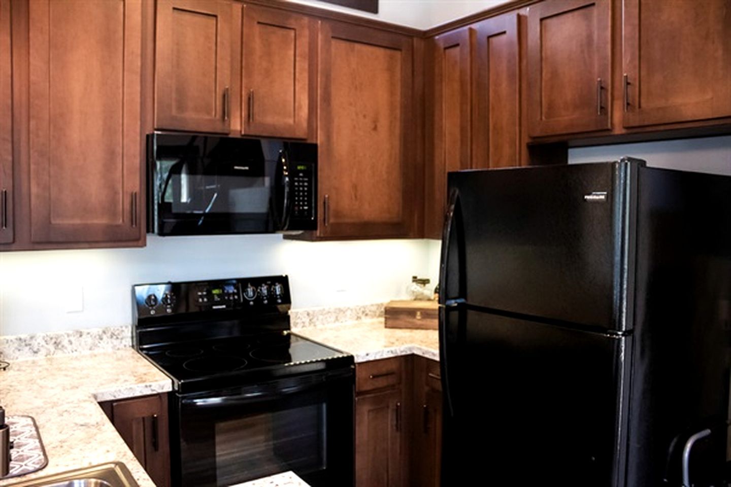 Una cucina con mobili in legno, un forno a microonde nero, un piano cottura nero e un frigorifero nero.