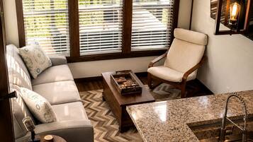 A modern living room with a sofa, armchair, coffee table, and a kitchen area with a granite countertop and sink.
