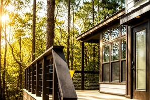 A modern building with large windows and a deck overlooking a forest.