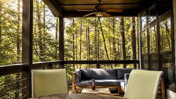 Une terrasse en bois avec un canapé et des fauteuils, donnant sur une forêt.