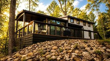 Eine moderne Hütte mit einer Terrasse, umgeben von felsigem Gelände und Bäumen.