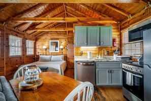 A cozy cabin interior with a wooden ceiling, a dining area with a table and chairs, a kitchenette with a stove and refrigerator, and a bed with a headboard. - Impressive Wooden Rustic Cabin with Fireplace in Mentone, Alabama (Mentone)