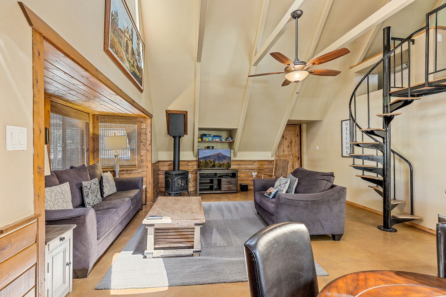 A spacious loft-style living area with a high ceiling, a fireplace, a television, and a spiral staircase.
