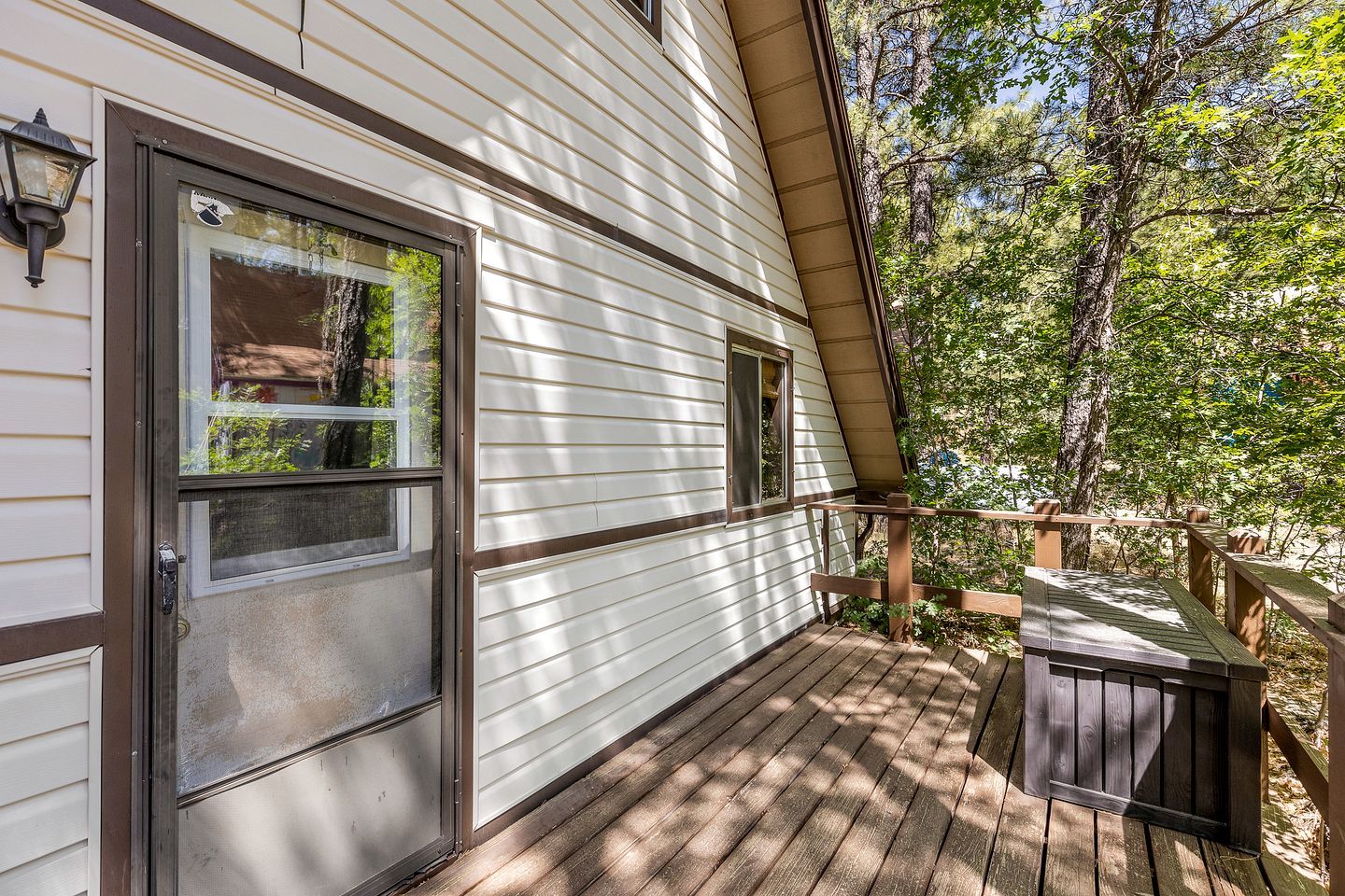A wooden deck with a metal railing, a door with a window, and a small outdoor seating area.