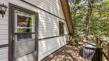 A wooden deck with a metal railing, a door with a window, and a small outdoor seating area.