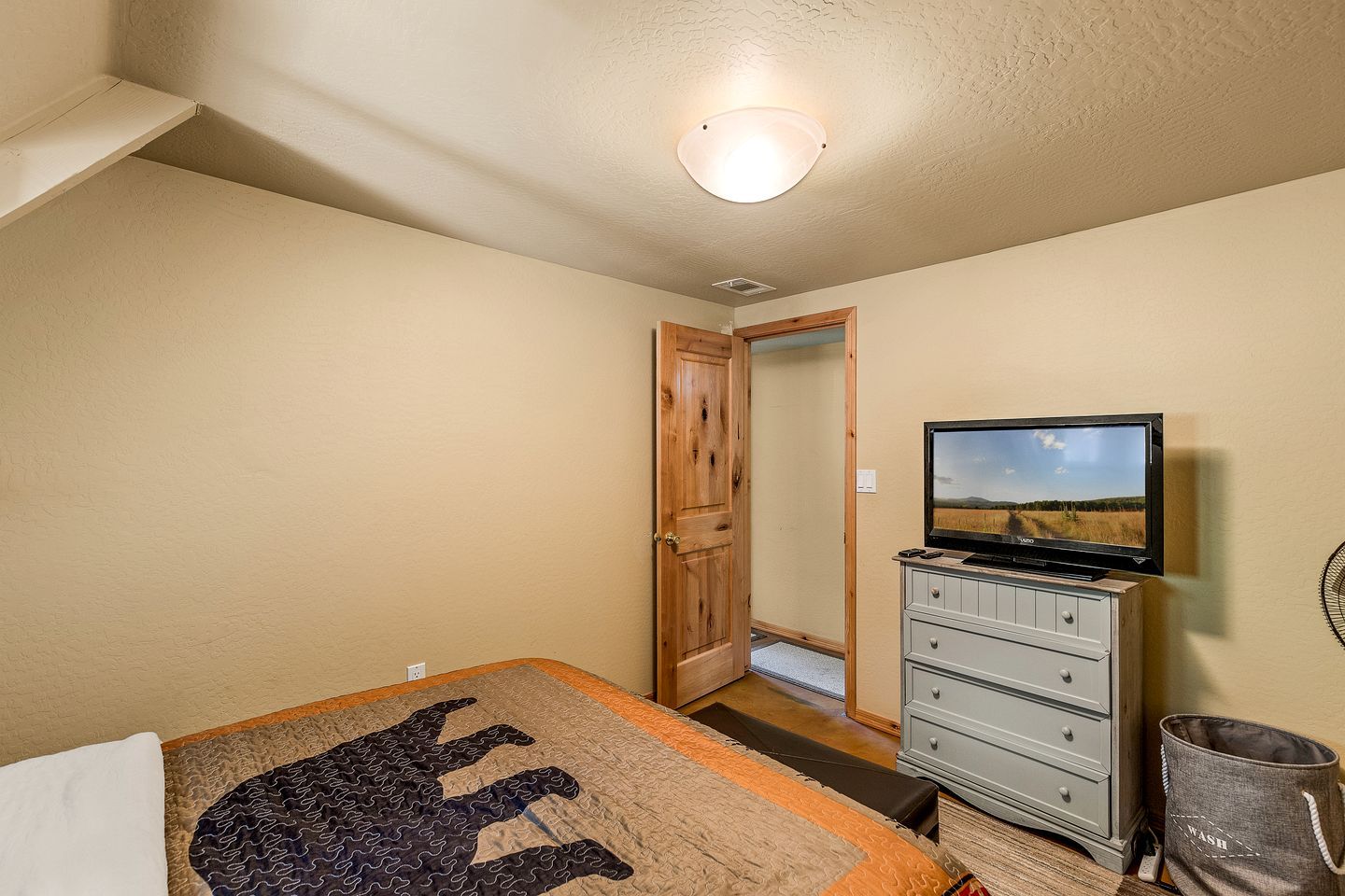 A bedroom with a bed, a dresser, a television, and a door leading to another room.